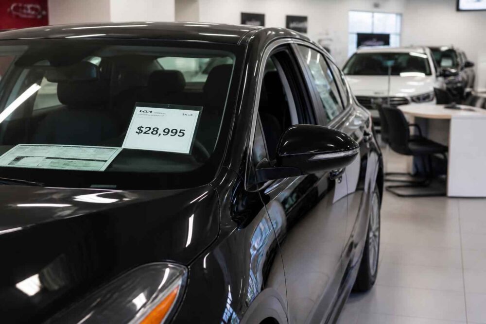 Czarny samochód z kartą cenową 28 995 dolarów na przedniej szybie w salonie dealerskim