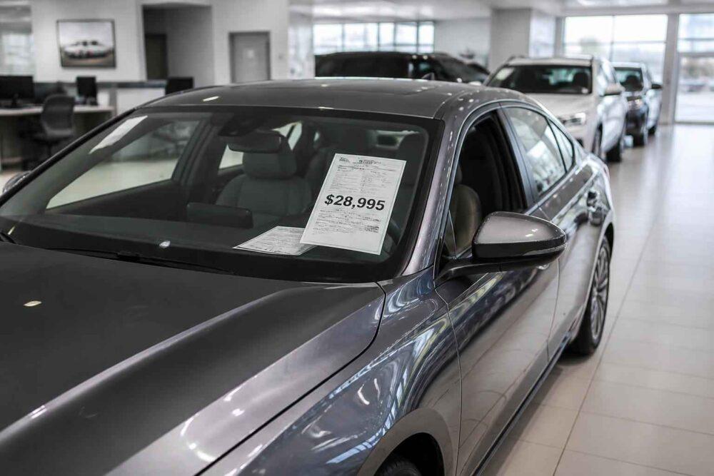 Czarny sedan z kartą cenową 28 995 dolarów w salonie samochodowym