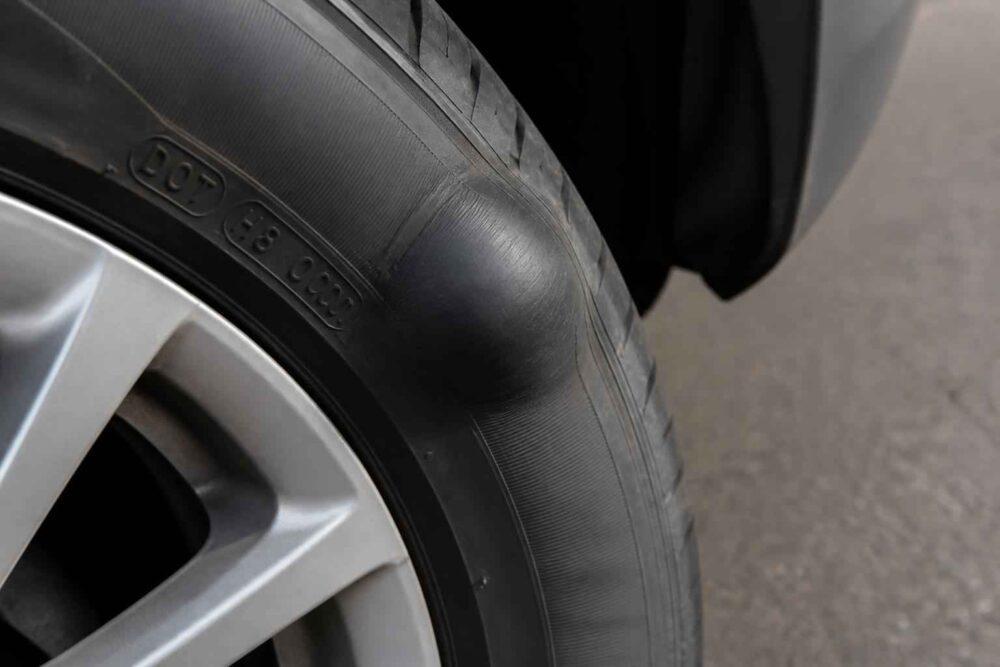 Zbliżenie na wybrzuszenie na boku opony samochodowej przy feldze aluminiowej