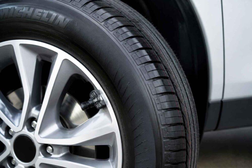 Srebrna felga aluminiowa z czarną oponą przy samochodzie
